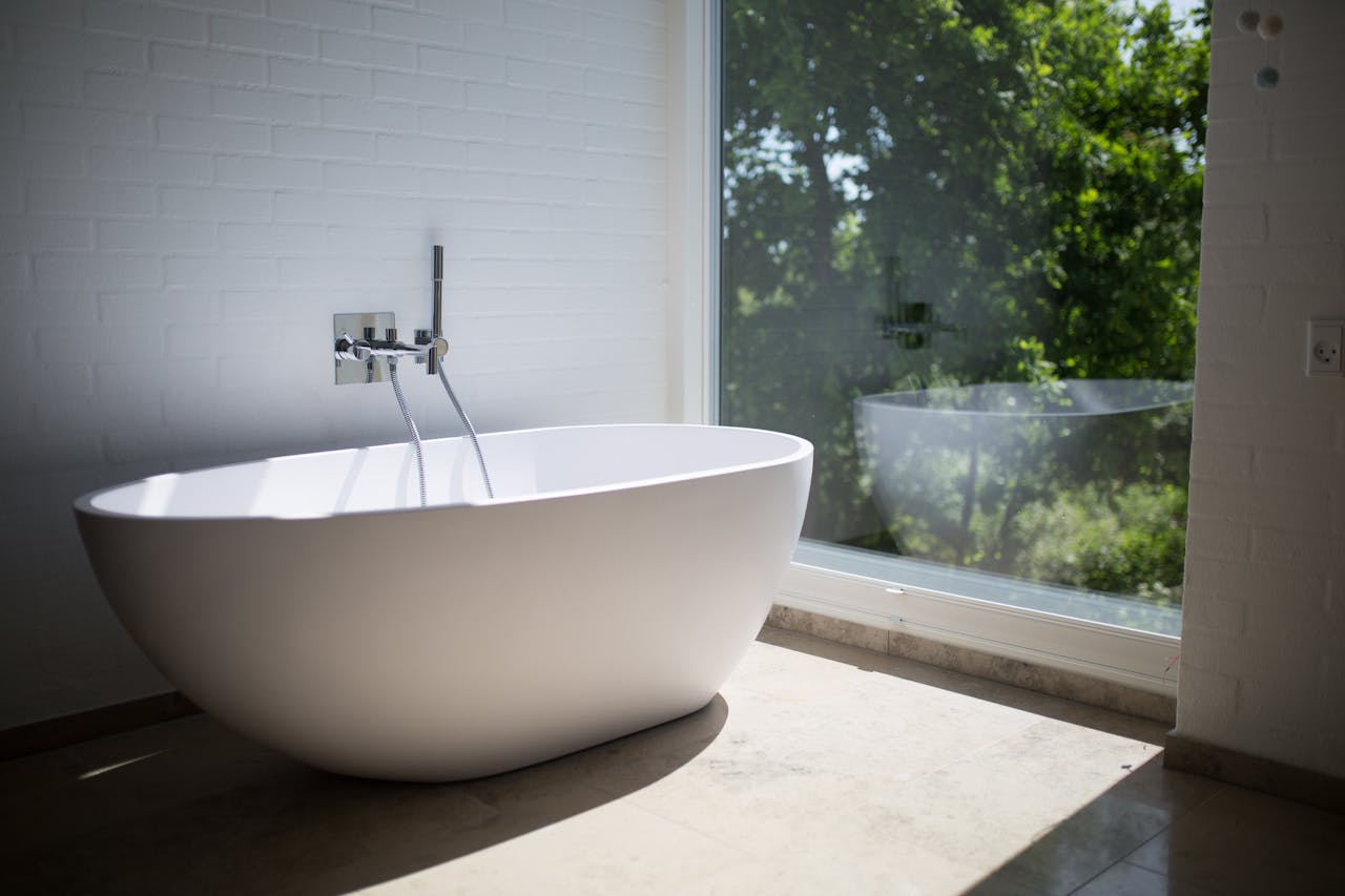 home-hero Sleek white bathtub by large window in sunlit minimalist bathroom setting.